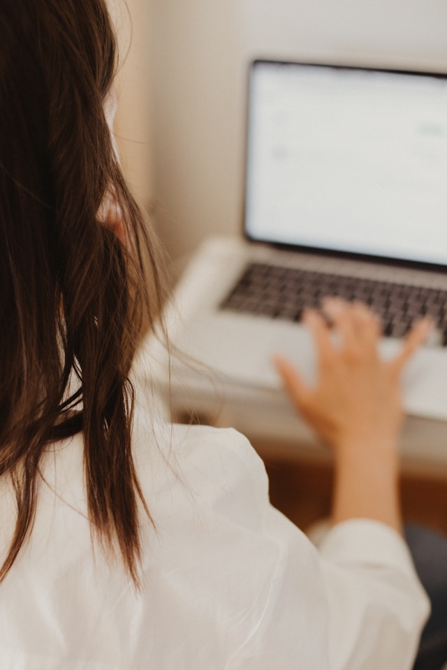 jeune femme brune de dos en train de faire une réclamation depuis son ordinateur portable